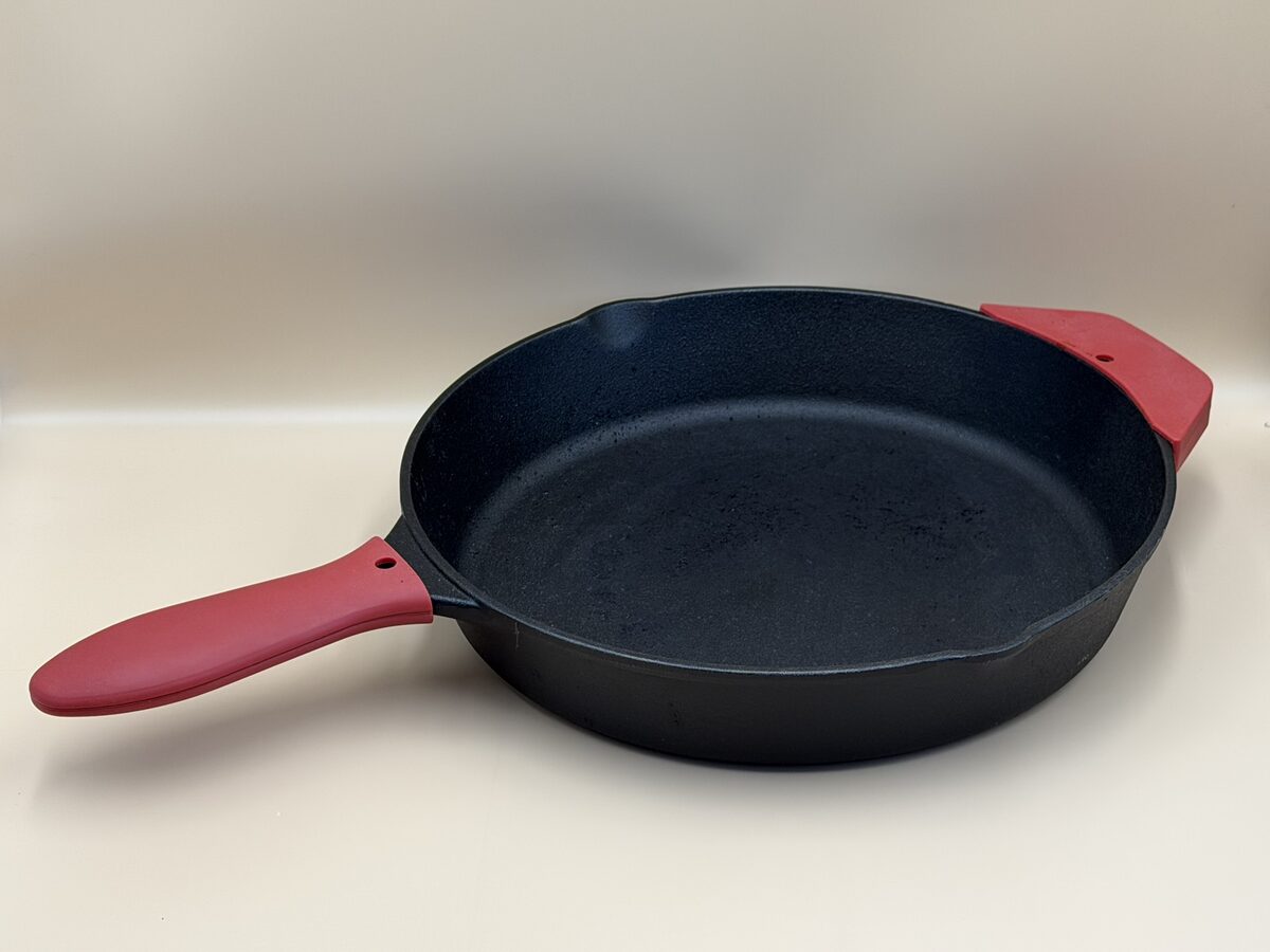 A 12-inch cast iron skillet with red silicone handle covers